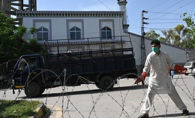 a plain clothes policeman wearing a facemask seals off a street with barbed wire at a residential area in islamabad as a preventive measure against the covid 19 photo afp file